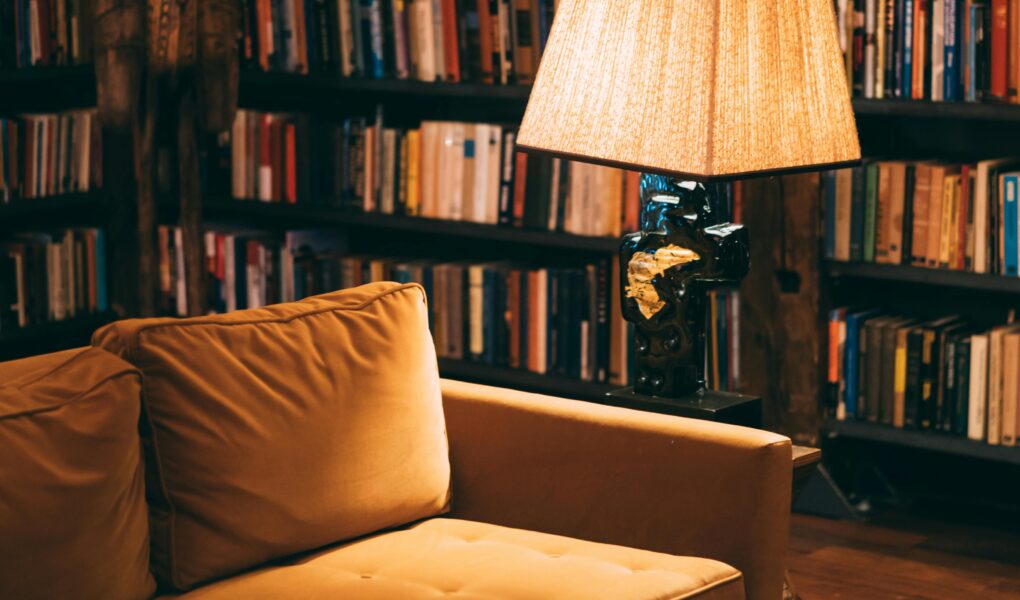A cozy reading nook, with low lighting, a couch, bookshelves, and a lamp.