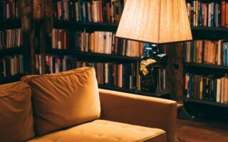 A cozy reading nook, with low lighting, a couch, bookshelves, and a lamp.