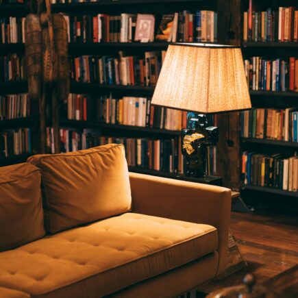 A cozy reading nook, with low lighting, a couch, bookshelves, and a lamp.