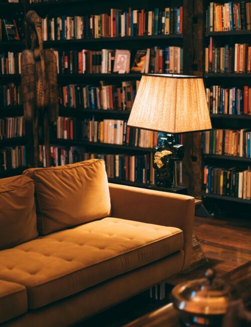 A cozy reading nook, with low lighting, a couch, bookshelves, and a lamp.
