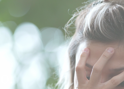 a woman holds her hand over her face, with trees and sunlight in the background