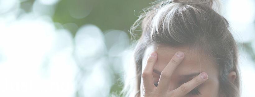 a woman holds her hand over her face, with trees and sunlight in the background